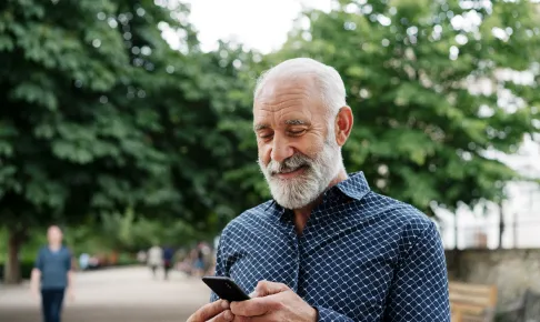 An elderly man — outdoors and smiling looking at his phone